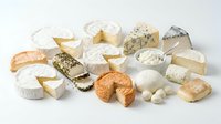 Assorted soft and aged cheeses with white rinds, fresh mozzarella balls, and crusty bread slices arranged on white background for culinary and food styling projects.