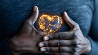 African American hands gently holding glowing heart shape made of golden light against dark background, representing love, care, and emotional connection.