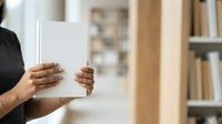 Woman holding blank white tablet device with both hands, displaying empty screen for mockup and app presentation purposes in modern home office setting.