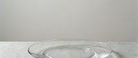 Empty clear glass bowl on white surface with neutral gray background, isolated for product display and design use.