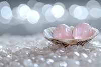 Pink rose quartz crystal spheres in decorative bowl on clear gemstones with soft bokeh lights background for healing meditation and wellness practices.
