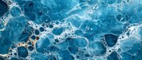 Ocean waves create natural foam and bubbles on deep blue water surface, abstract aerial panoramic view showing dynamic sea movement and white seafoam patterns.