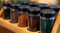 Glass spice jars filled with colorful herbs and seasonings arranged on wooden shelf for cooking and culinary preparation in kitchen pantry storage.