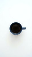 Blue ceramic coffee mug with black coffee viewed from above on white background. Minimalist morning beverage concept for cafe and kitchen designs.