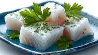 Fresh white fish fillet cubes garnished with green parsley on blue ceramic plate. Raw seafood preparation for sushi, sashimi or cooking recipes.