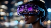 Young African American woman wearing virtual reality headset with purple city reflection, experiencing immersive technology against blurred night cityscape background.