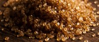Brown sugar crystals scattered on dark wooden surface with warm lighting and shallow depth of field for baking and culinary projects.