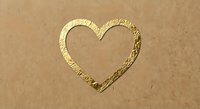 Golden heart shape drawn in sand on beach surface with textured outline and smooth interior for romantic designs and love concepts.