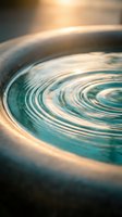 Swirling water ripples create mesmerizing circular patterns in ceramic bowl with warm golden lighting and turquoise blue tones for meditation and wellness concepts.