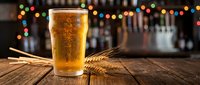Fresh golden beer in glass with wheat stalks on wooden bar counter with colorful bokeh lights background for brewery and pub atmosphere.