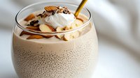 Creamy chia pudding topped with whipped cream, sliced banana, nuts and chocolate drizzle in glass bowl. Healthy breakfast dessert recipe concept.