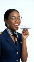 Happy African American female pilot in uniform holding paper airplane on white background for aviation and travel concepts.