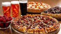 Fresh pizzas with various toppings served alongside craft beer glasses and bowl of raspberries on wooden table, appetizing restaurant food photography.
