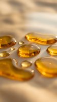 Golden amber gel capsules and liquid droplets on neutral surface, suitable for pharmaceutical, wellness, supplement and healthcare marketing materials.