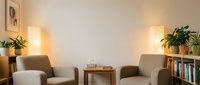 Cozy modern living room interior with two beige armchairs, wooden coffee table, warm lighting and green plants creating comfortable home atmosphere.