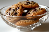 Fresh baked chocolate chip cookies in clear glass bowl, showing crispy golden edges and melted chocolate morsels, close-up food photography.