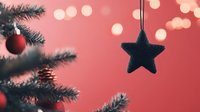 Festive black star ornament hanging against pink bokeh background with Christmas tree branch and red bauble, creating magical holiday atmosphere.