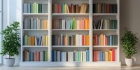 Modern white bookcase with colorful books arranged by spectrum, flanked by potted green plants in bright interior space.