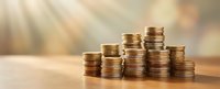 Growing stacks of golden coins on wooden surface with warm sunlight rays creating financial growth and investment success concept for business.