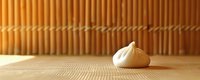 Single white meringue cookie on textured bamboo mat against warm wooden background with soft natural lighting and minimalist composition.