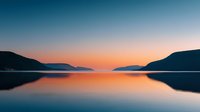 Serene mountain lake at sunset with calm waters reflecting orange and pink sky colors creating peaceful landscape scenery for relaxation and nature themes.