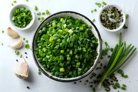 Fresh chopped green onions in black bowl with garlic cloves and peppercorns on light background, top view of healthy cooking ingredients.