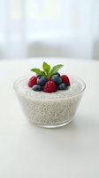 Chia seed pudding topped with fresh blueberries, raspberries and mint leaves in glass bowl on white surface for healthy breakfast and superfood recipes.