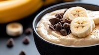 Fresh banana smoothie bowl topped with chocolate chips and sliced bananas in black ceramic bowl. Healthy breakfast or dessert with creamy texture.