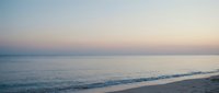 Serene ocean waves gently rolling onto sandy beach at twilight with soft pastel sky colors creating peaceful coastal atmosphere for relaxation and meditation.