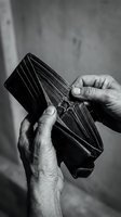 Elderly hands holding empty worn leather wallet showing financial hardship and poverty in dramatic black and white photography for social awareness campaigns.