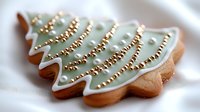 Festive Christmas tree sugar cookie decorated with mint green royal icing and gold pearl sprinkles on white background, holiday baking and food photography.