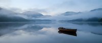 Serene mountain lake at dawn with wooden boat floating on calm reflective water surrounded by misty hills and soft morning light creating peaceful atmosphere.