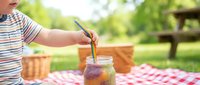 Young child in striped shirt pouring fresh lemonade into glass jar at outdoor picnic table on sunny day, summer refreshment and family gathering concept.