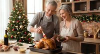 Senior Caucasian couple preparing Christmas turkey dinner together in festive kitchen with decorated tree, holiday cooking and family traditions.