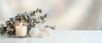 Minimalist spa wellness setup with burning candle, rose quartz crystals and eucalyptus branches on white surface against soft neutral background for relaxation.