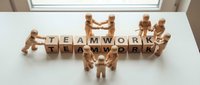 Wooden figurines arranged in a circle around letter blocks spelling teamwork and teamwork, symbolizing collaboration, unity, and cooperative business success on white surface.