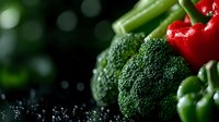 Fresh raw vegetables with water drops on dark background. Bright red bell peppers, green broccoli florets and celery stalks in moody lighting with bokeh effect.
