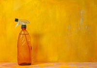 Orange plastic spray bottle against vibrant yellow wall background, minimalist composition with copy space for cleaning or household concepts.