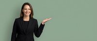 Professional businesswoman in black suit presenting with open palm gesture against sage green background for corporate marketing materials.