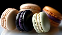 Colorful French macarons with smooth shells and creamy filling arranged on dark background. Assorted flavors including chocolate, vanilla, pistachio pastries.