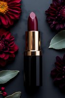Burgundy lipstick with gold metallic case on dark background surrounded by deep red dahlias and green leaves, luxury cosmetic product photography.