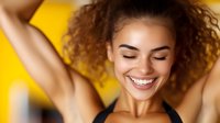 Young woman with curly hair expressing joy and freedom against yellow background, showing genuine happiness and positive emotions for lifestyle and wellness content.