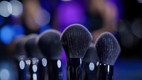 Professional makeup brushes on dark background with purple and blue bokeh lights creating luxurious cosmetic atmosphere for beauty industry advertising.