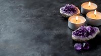 Glowing tea light candles alongside purple amethyst crystal clusters and geodes on dark textured background, creating serene spa atmosphere for meditation and wellness.