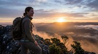 Hiker with backpack standing on rocky mountain peak at sunrise overlooking misty valley landscape below, adventure and outdoor exploration concept for travel and nature themes.