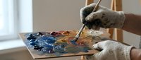 Artist hand holding paintbrush mixing colors on palette in bright studio workspace for creative painting project and artistic expression.