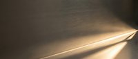 Warm sunlight streaming through window creating dramatic light rays and shadows on textured wall surface for interior design and architectural concepts.