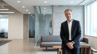 Confident middle-aged Caucasian male executive posing in modern corporate office lobby, wearing dark blazer, professional business portrait.