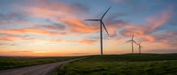 Wind turbines on green hills at sunset with dramatic orange and pink sky clouds. Renewable energy landscape with rural road for sustainable power concepts.