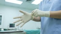 Medical professional putting on sterile latex gloves in operating room preparing for surgery or medical procedure in hospital environment.